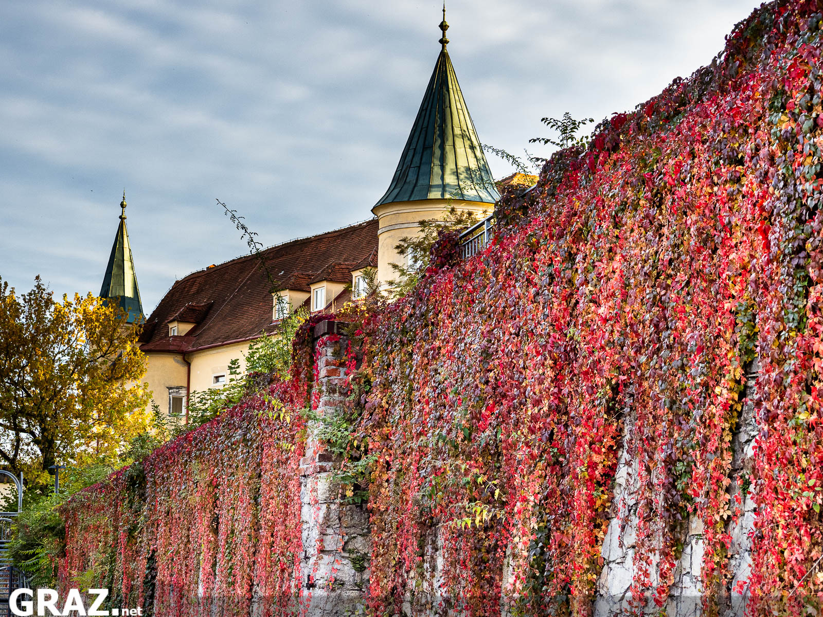 Rotes Herbstlaub an einer langen Mauer vor den Türmen von Schloss St. Martin in Graz