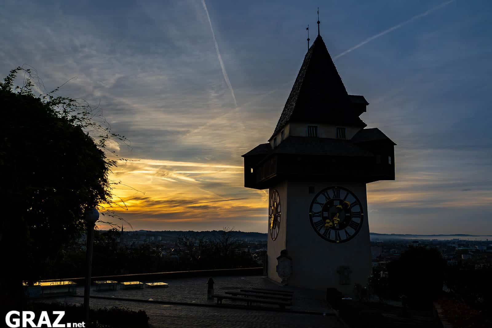 Dunkle Silhouette des Grazer Uhrturms vor dem ersten goldenen Morgenlicht über der Stadt