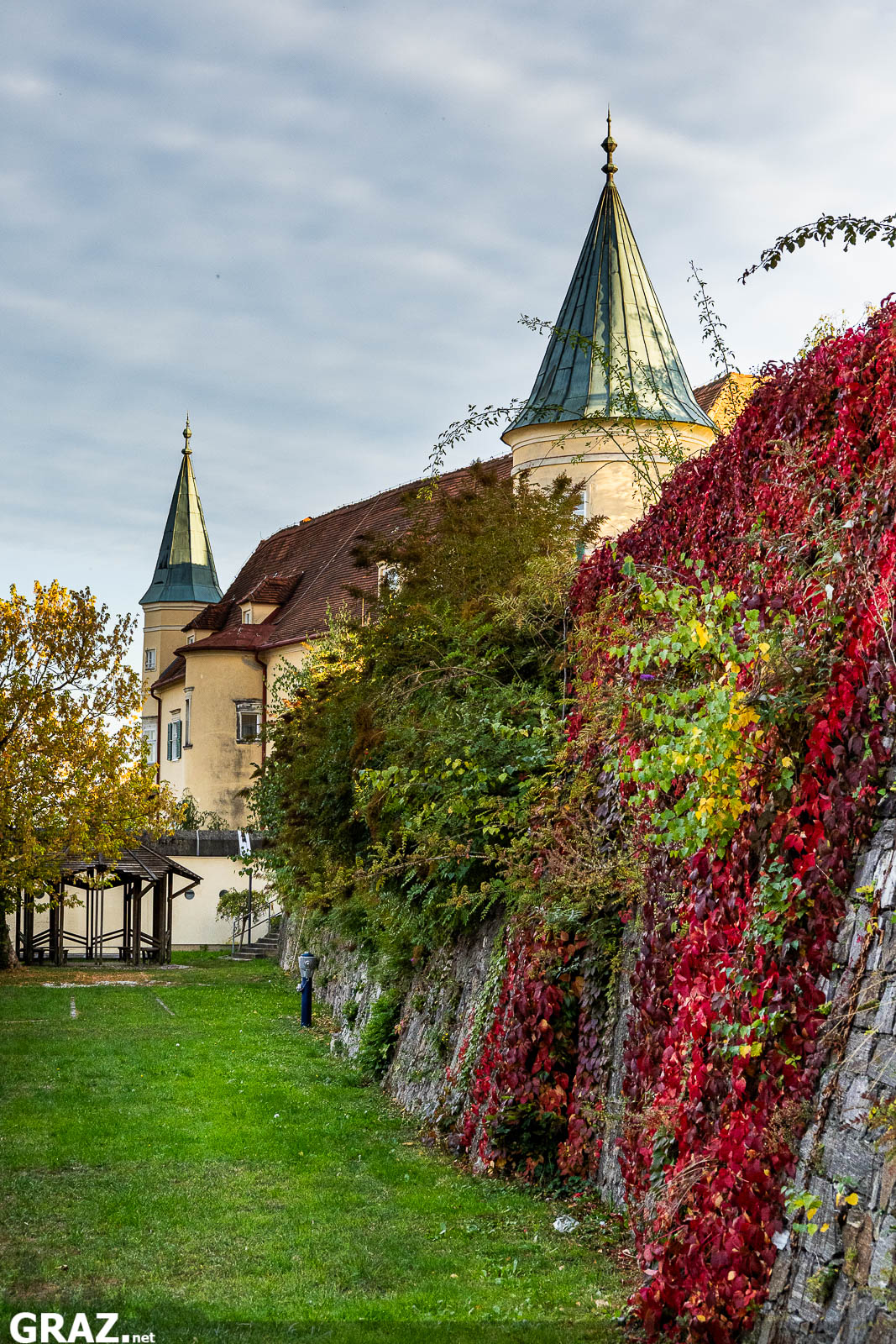 Schloss St. Martin mit grünem Turmdach hinter einer rot bewachsenen Mauer und einem Wiesenstreifen