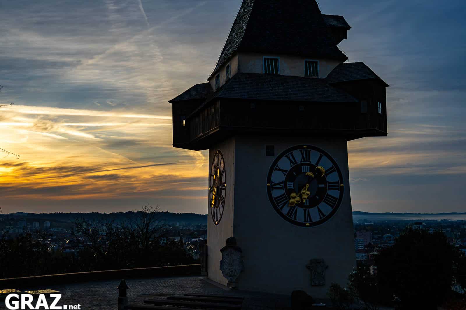 Uhrturm am Grazer Schloßberg mit sichtbarem Zifferblatt vor orange leuchtenden Morgenwolken