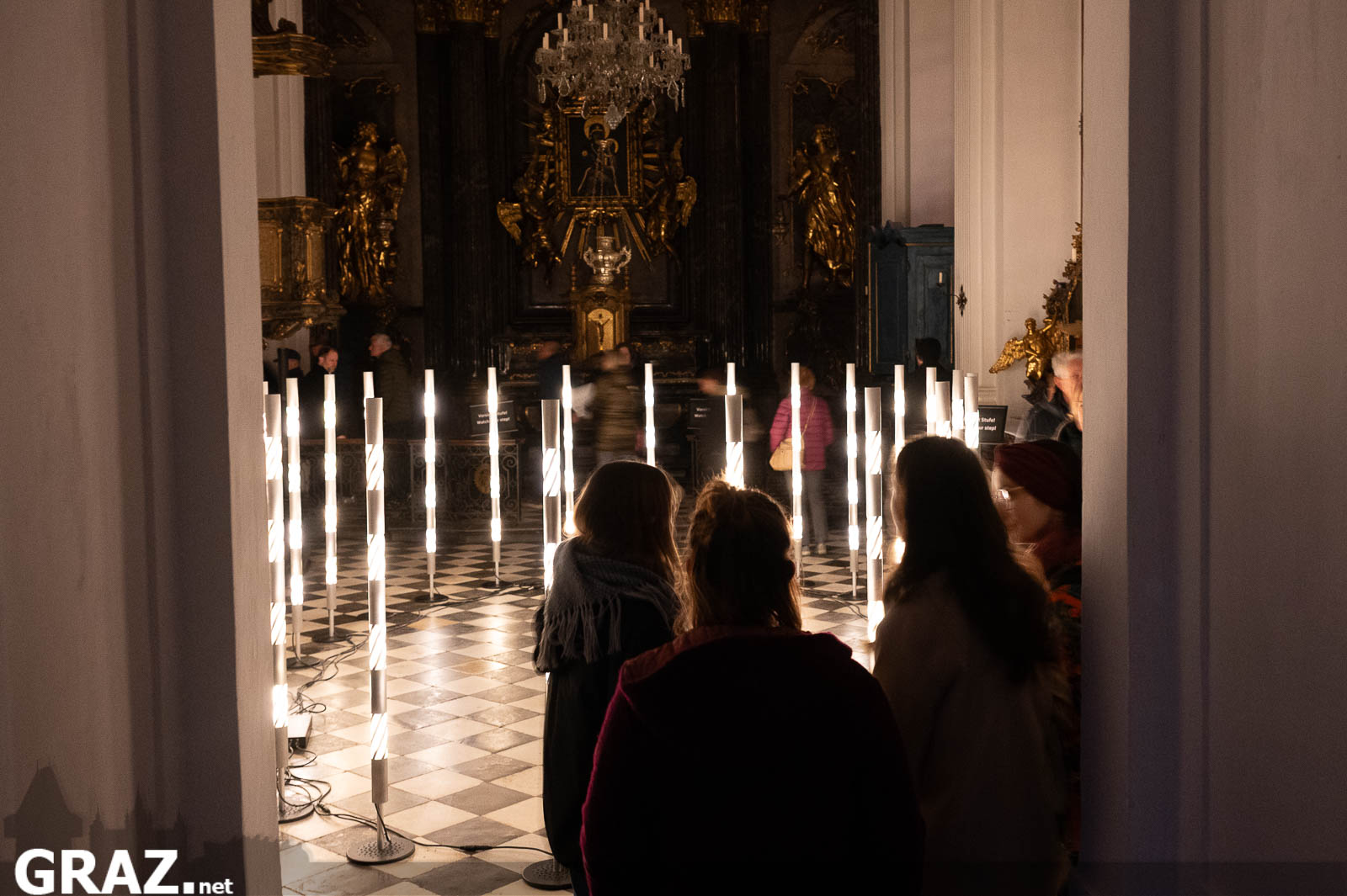 Zwei Gäste blicken durch den Eingang der Schlosskapelle auf die Lichtinstallation „Continuum“ von Robin Beekman.