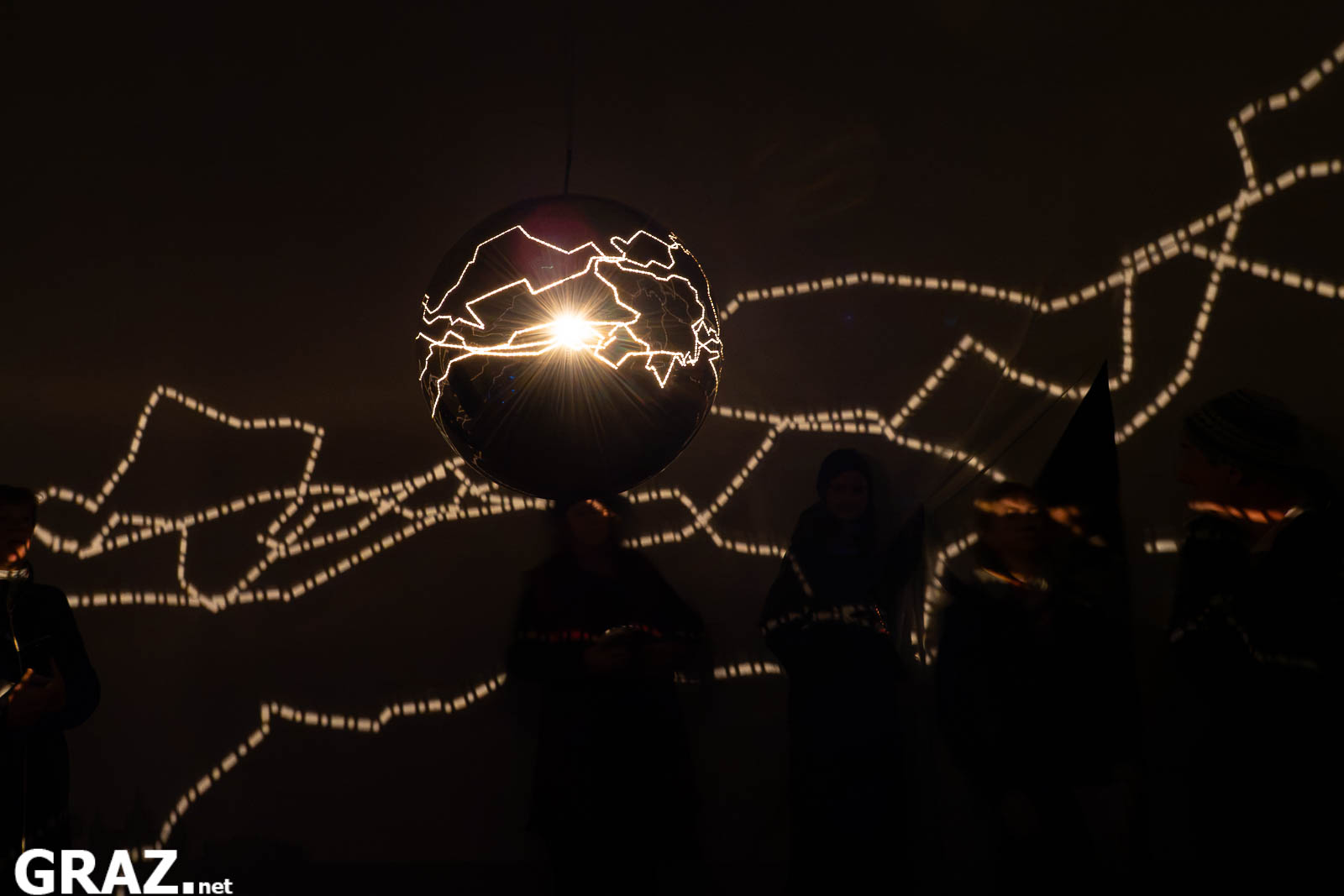 Gäste stehen unter der leuchtenden Kugel von Helga Griffiths’ „Migratory Senses“; Lichtlinien ziehen sich über die Wand.