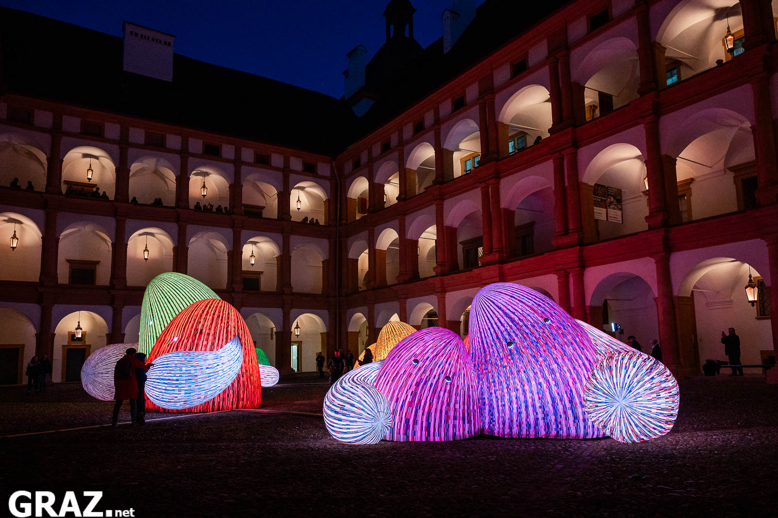Die „Whispering Mountains“ von ENESS leuchten rosa, blau und grün vor den Arkaden von Schloss Eggenberg.