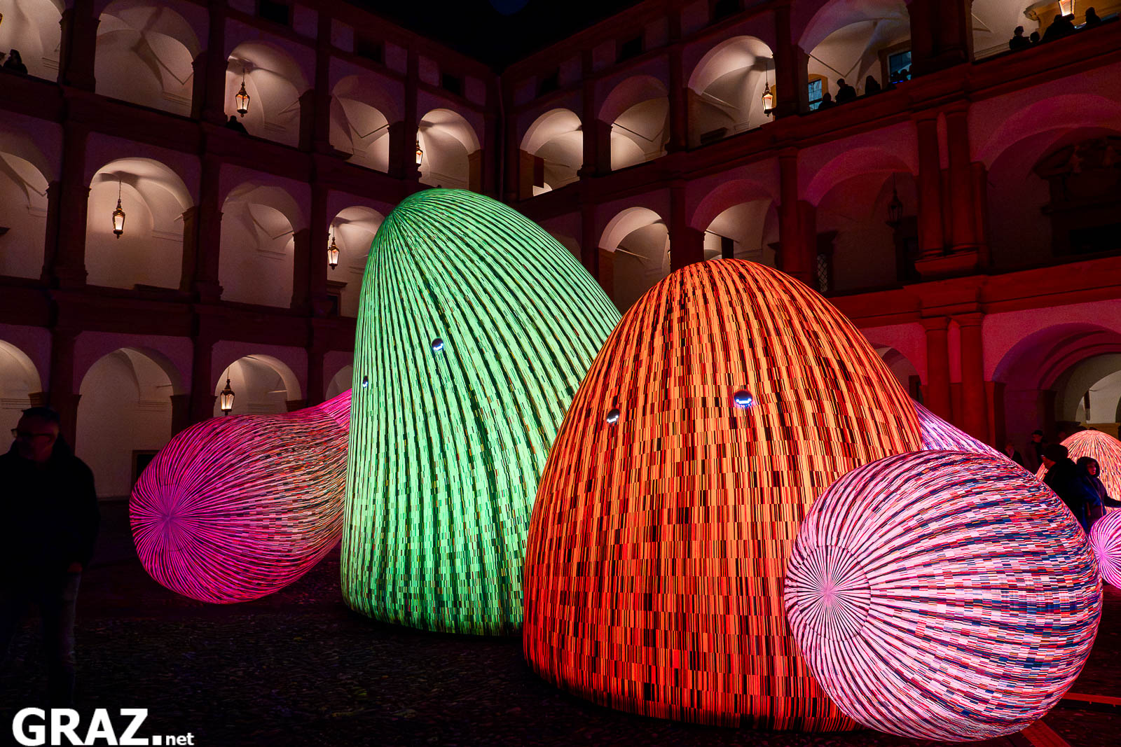 Grün und orange leuchtende Bergfiguren aus „Whispering Mountains“ von ENESS im Schlosshof Eggenberg.