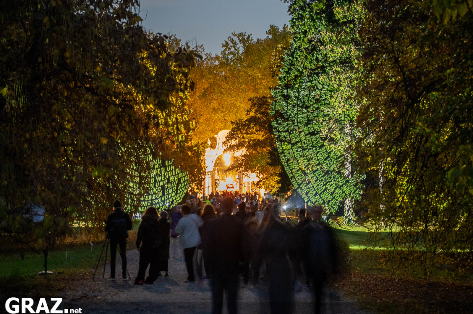 Gäste gehen durch die mit Textprojektionen von „Räume der Zeit“ von Hartung & Trenz beleuchtete Allee zum Schloss Eggenberg.