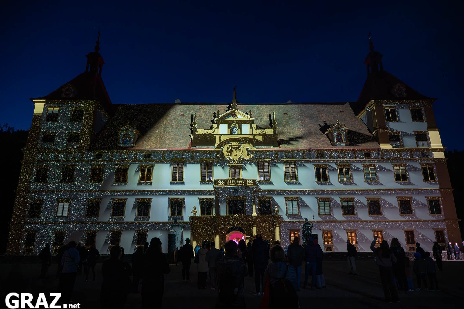 Daniel Rossas „Kadenzen“ legt helle Projektionen über die Fassade von Schloss Eggenberg; davor steht das Publikum.