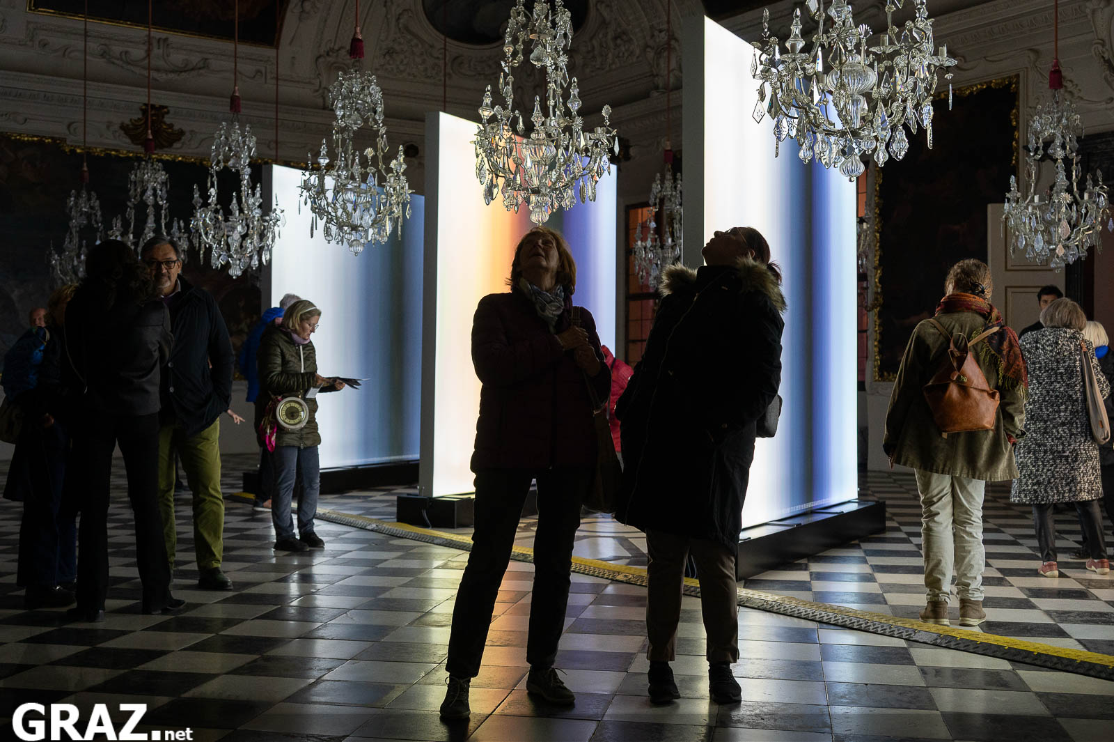 Gäste betrachten Inge Dicks „jahres licht weiss“ zwischen den Kronleuchtern des Planetensaals in Schloss Eggenberg.
